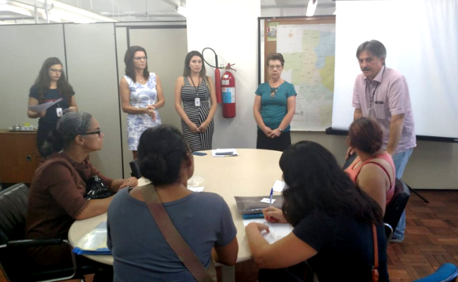 Quatro pessoas em pé e outras três sentadas no entorno de uma mesa
