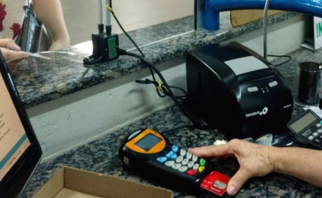 Em um guichê, uma atendente mexe uma máquina de cartões