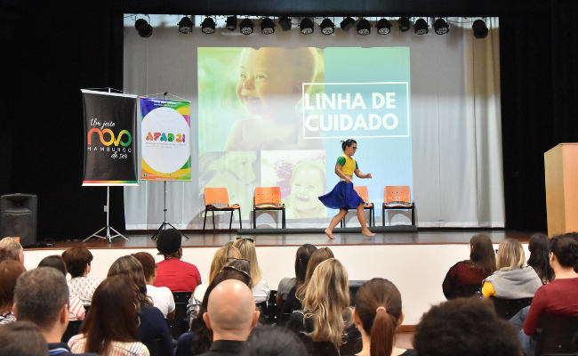 Menina dança em um palco enquanto platéia sentada assiste