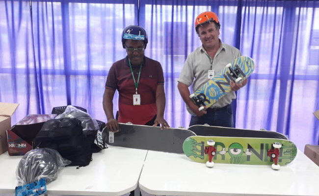 Dois homens em pé, com skates em uma mesa à frente
