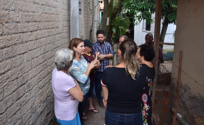 Em um beco, a prefeita em pé conversa com moradores