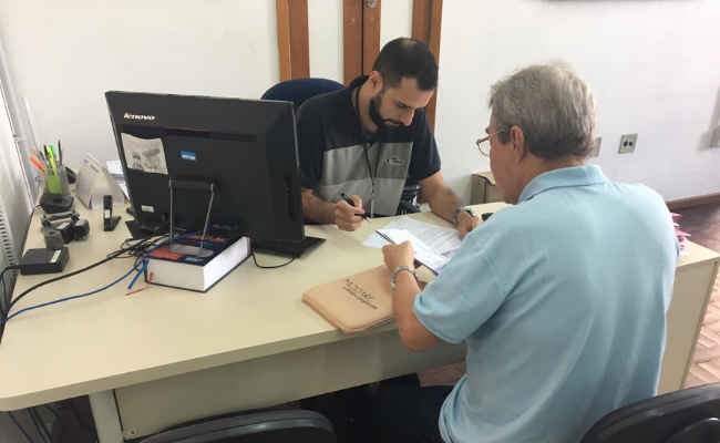 Dois homens sentados, um de cada lado de um mesa, com um computador em cima dela