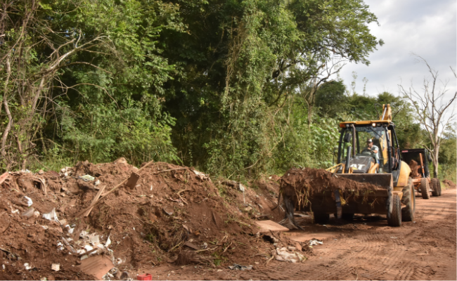 Um retroescavadeira faz a limpeza de entulhos no acostamento de um estrada
