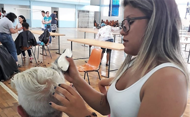 Menina em pé corta o cabelo de um menino sentado
