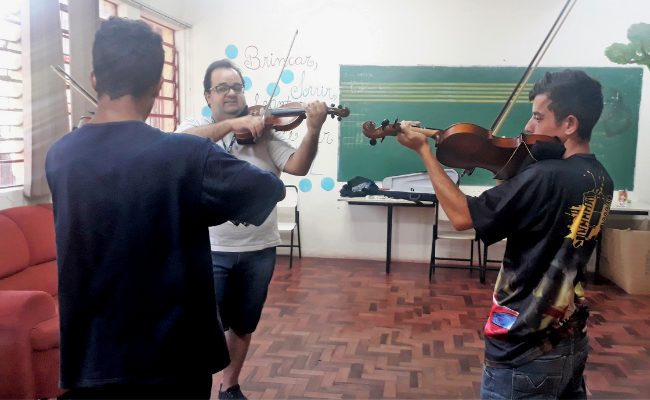 Três pessoas em uma sala tocando violino