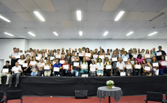 Em um palco, os 92 homenageados seguram os certificados de reconhecimento
