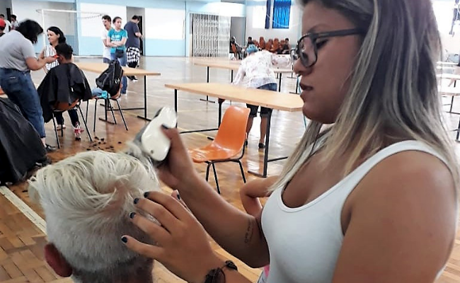 Jovens em pé corta o cabelo com uma máquina de um menino sentado
