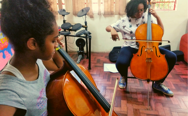 Duas meninas sentadas tocando violoncelo em uma sala