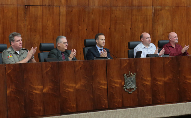 Cinco homens sentados em uma tribuna, com o vice-prefeito sentado na ponta direita