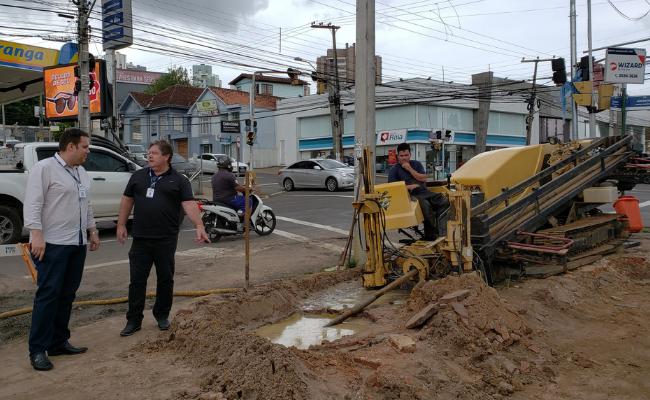 Dois homens em pé ao lado de um máquina que faz um furo no chão