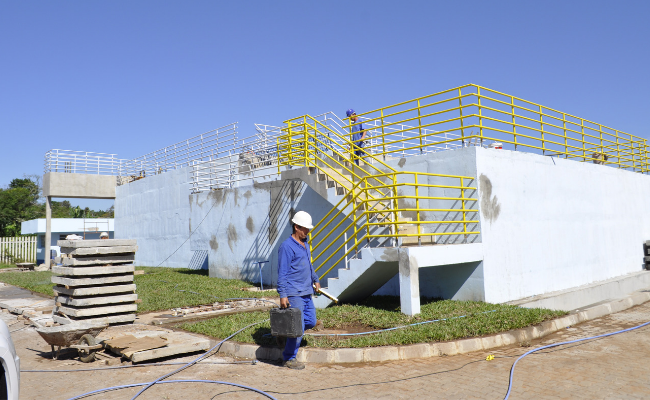 Ao fundo, a estação de tratamento em construção. À frente, um operário trabalhando