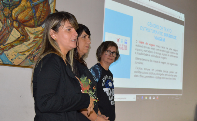 Três mulheres em pé com uma projeção atrás delas