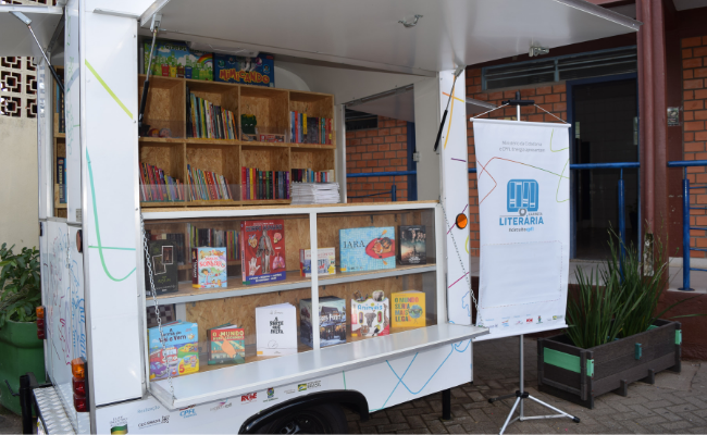 Uma carreta branca com um janela no lado, que permite a visualização dos livros em estandes