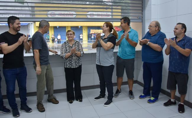 Dentro de uma banca, a prefeita em pé no meio e pessoas ao seu entorno