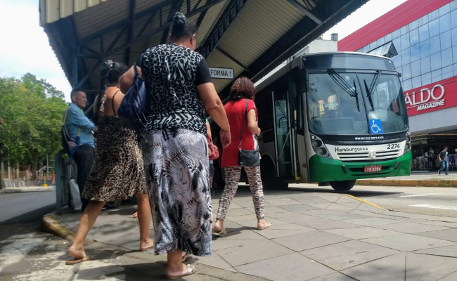 Em uma grande parada de ônibus, o coletivo está parado e pessoas embarcando