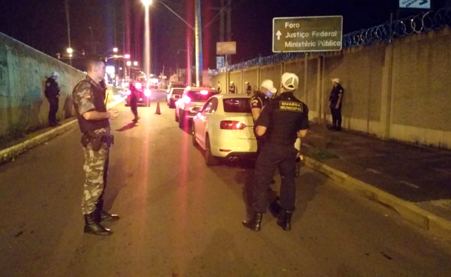 Em uma rua, dois policiais em pé com um carro estacionado