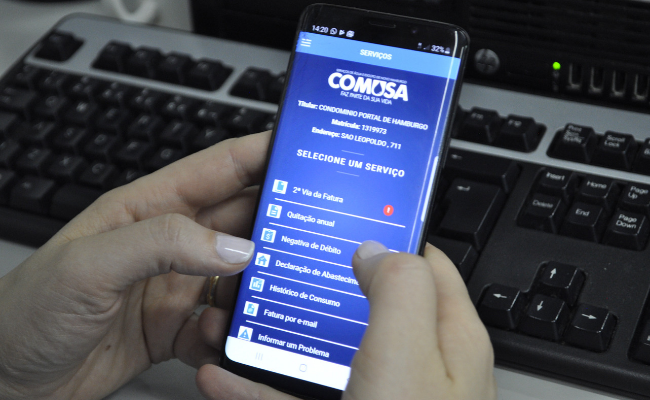 Duas mãos segurando um celular com um teclado de computador embaixo