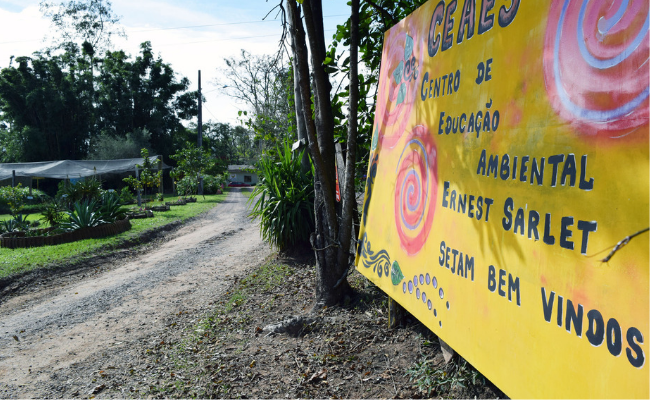 À direita, uma placa grande amarela com o escrito Centro de Educação Ambiental recebe a comunidade