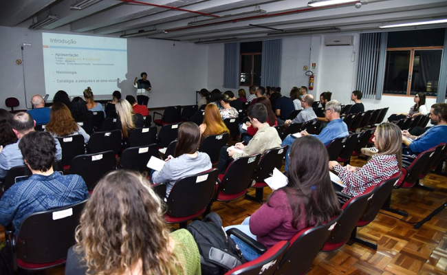 Em uma sala, grupo de pessoas sentadas em cadeiras