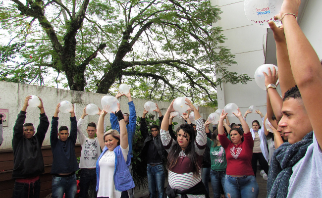 Grupo de pessoas com os braços erguidos segurando um balão branco
