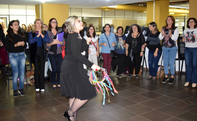 No saguão da Prefeitura, um grupo de pessoas formam um círculo. Ao centro deste círculo, uma mulher dança