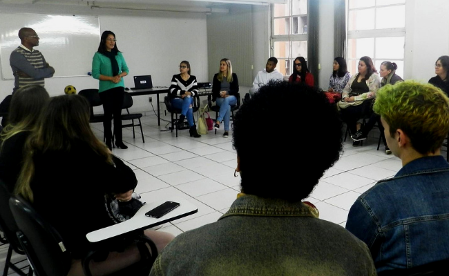 Em uma sala, grupo de pessoas sentadas em cadeiras em círculo