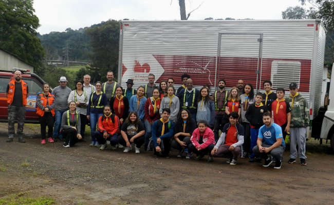 Grupo de pessoas lado a lado posando para a foto, com um caminhão atrás