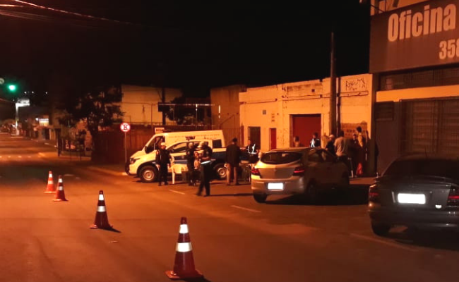 Em uma rua de asfalto, cones no meio da via e carros estacionados à direita sendo vistoriados pela Guarda Municipal