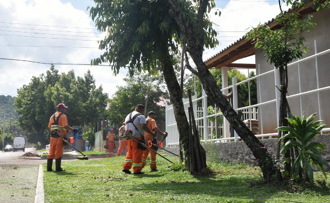 Em uma calçada, três homens de laranja cortar a grama com cortadores elétricos