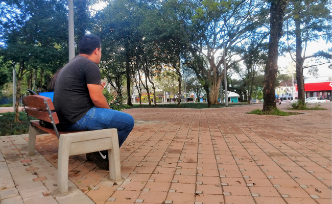 Um homem sentado em um banco na Praça do imigrante