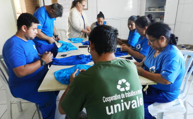 Quatro pessoas sentadas no entorno de uma mesa fazendo sacolas