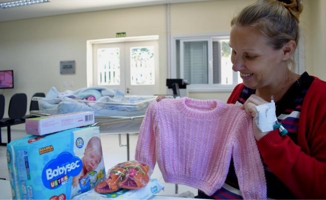 Mulher segurando uma roupa de bebê dentro da maternidade