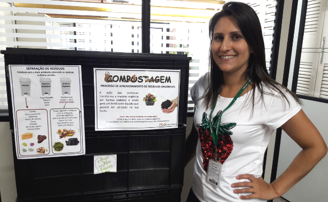 Uma mulher em pé ao lado de uma caixa grande preta (composteira)