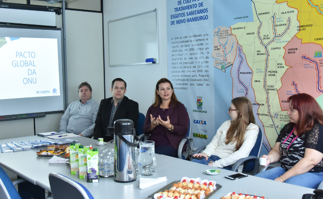 Sentados lado a lado em uma mesa, dois homens e três mulheres, sendo a prefeita que está no meio