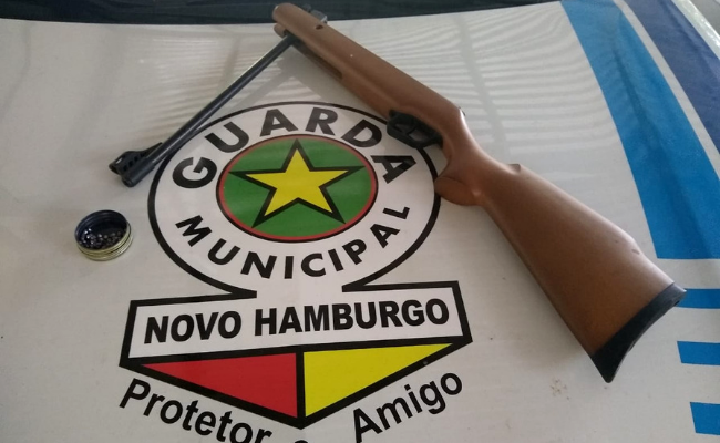 Uma arma de pressão em cima do capô de um carro com a insígnia da Guarda Municipal