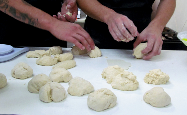 Dois jovens fazendo pães em cima de uma mesa