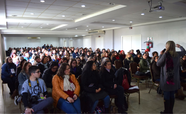 Em um auditório, público sentado e palestrante em pé
