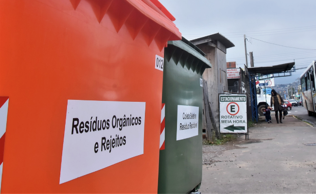 Um coletor laranja e um coletor verde lado a lado em uma rua