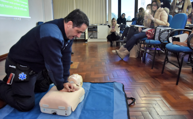 Em uma sala, homem simula massagem cardíaca em um boneco no chão