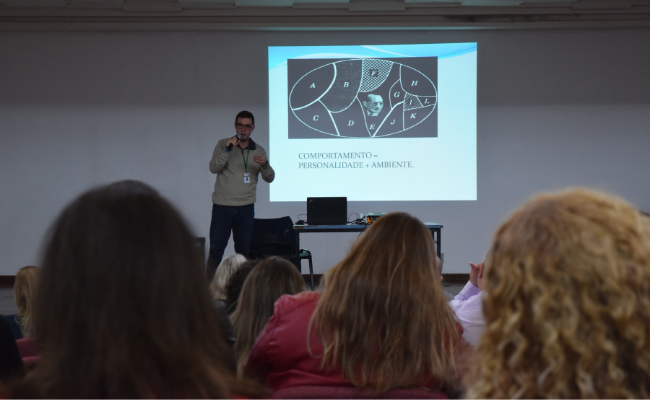Homem com um microfone em cima de um palco com pessoas sentadas