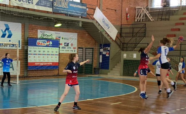 Em uma quadra esportiva, meninas jogam handebol