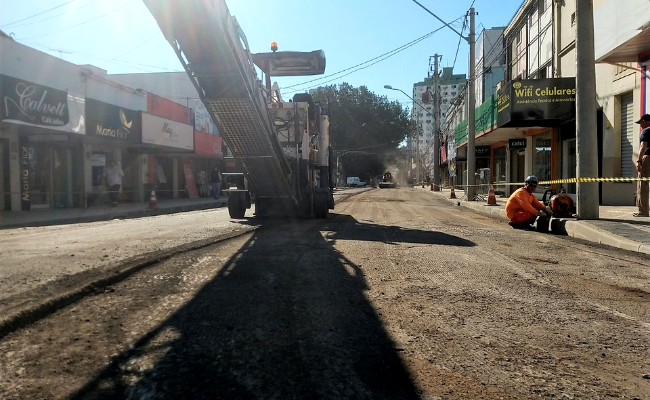 Em uma rua, um grande equipamento raspa o asfalto da via