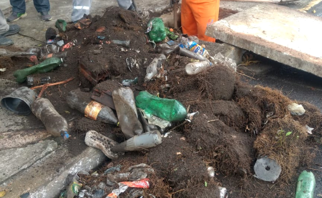 Ao lado de um bueiro em uma rua, um monte de garrafas de plástico e sujeira
