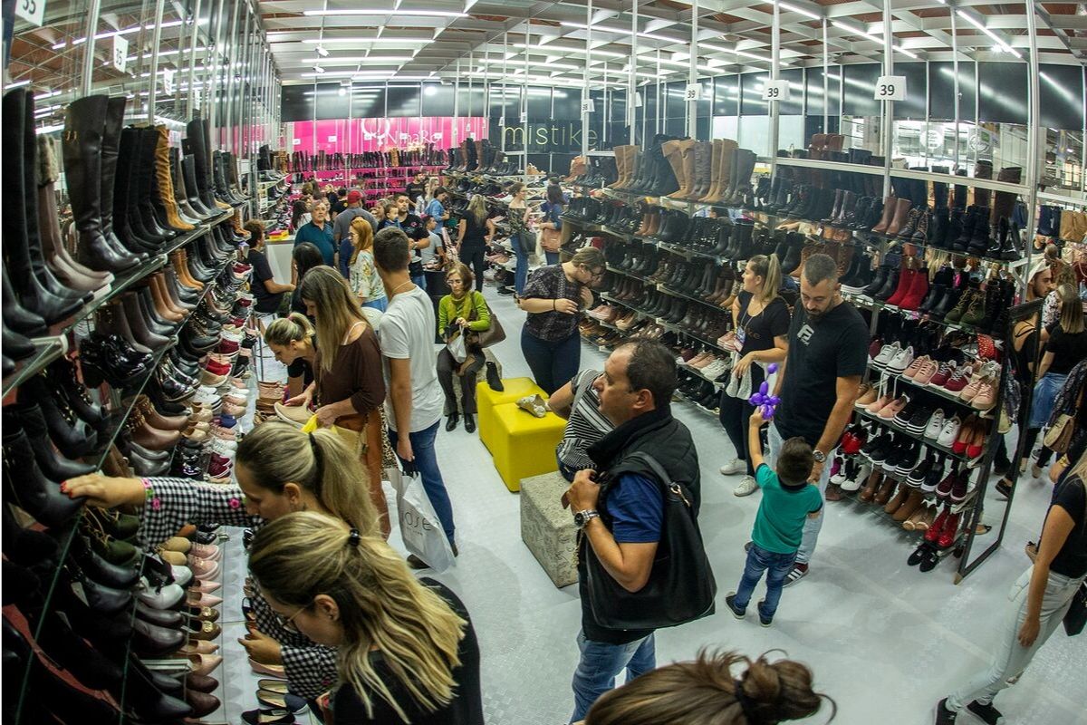 Dentro de um loja, estande nos dois lados repletas de sapatos e pessoas olhando os produtos