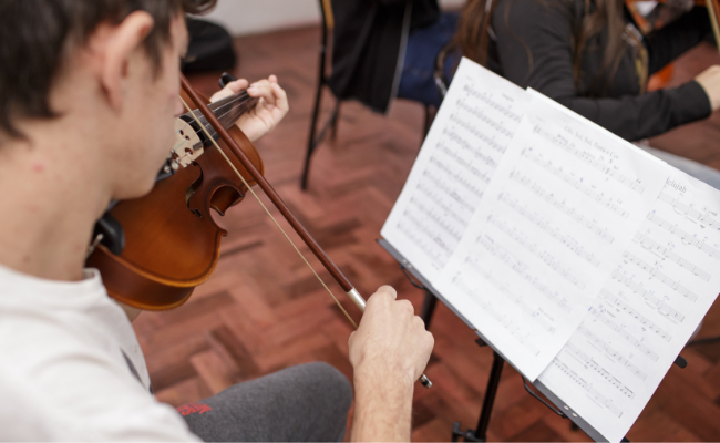 Menino sentado em um violino com um caderno de partitura a sua frente