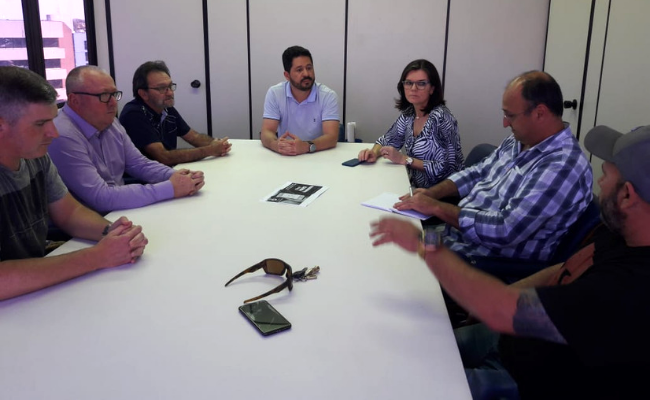 Em um sala, sete pessoas sentadas no entorno de uma mesa