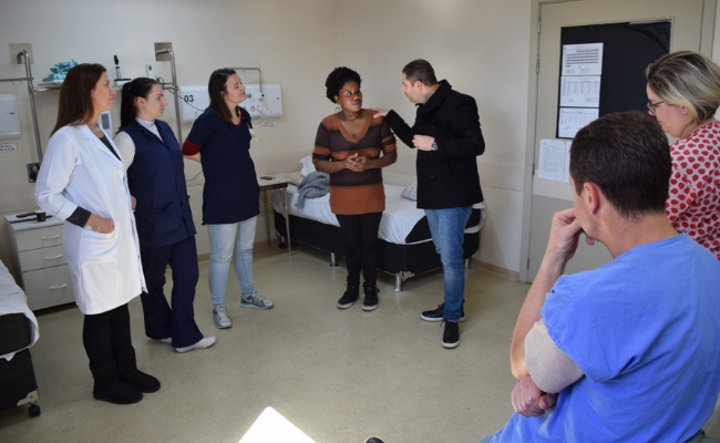 Em uma sala do Hospital, sete pessoas em pé formando um semicírculo conversando