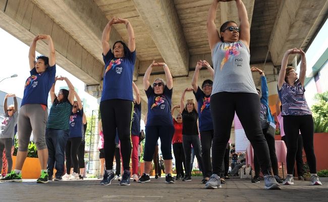 Em uma área aberta, pessoas organizadas em filas fazem exercícios