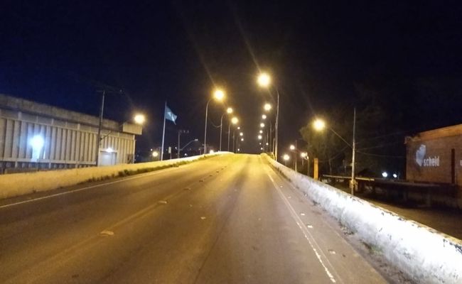 Imagem de uma rua asfaltada com iluminação em postes nos dias lados
