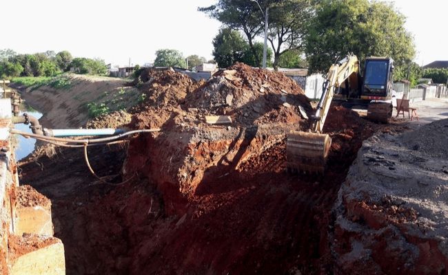 Máquina escavando uma área de terra ao lado da ponte